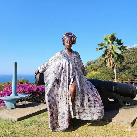 Woman in a kaftan standing next to a cannon with a scenic background