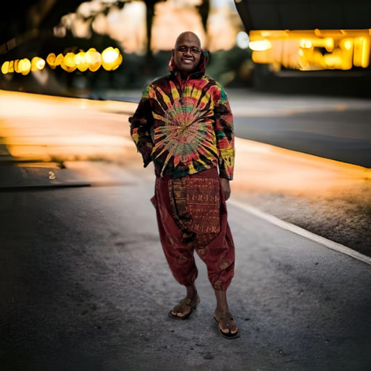 Person wearing a tie-dye hoodie and harem pants standing on a street with blurred lights in the background
