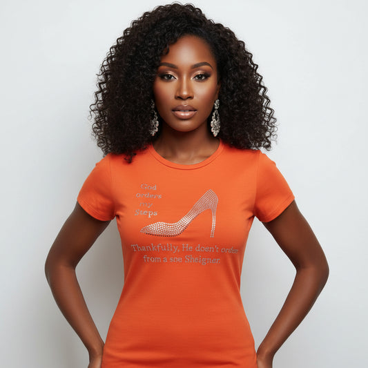 Woman wearing an orange cotton tee with "God orders my Steps" and a rhinestone stiletto design.