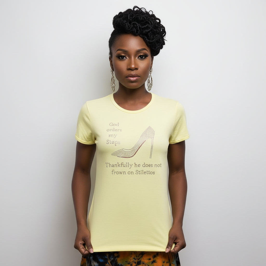Woman modeling a light yellow "God Orders My Steps" rhinestone stiletto t-shirt.