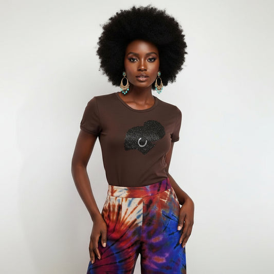 Woman in brown t-shirt with black rhinestone afro design, colorful tie-dye pants, and earrings.