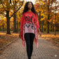 Woman walking on a path in an autumn park wearing a red and black patterned schawl