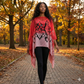 Woman walking on a path in an autumn park wearing a red and black patterned schawl
