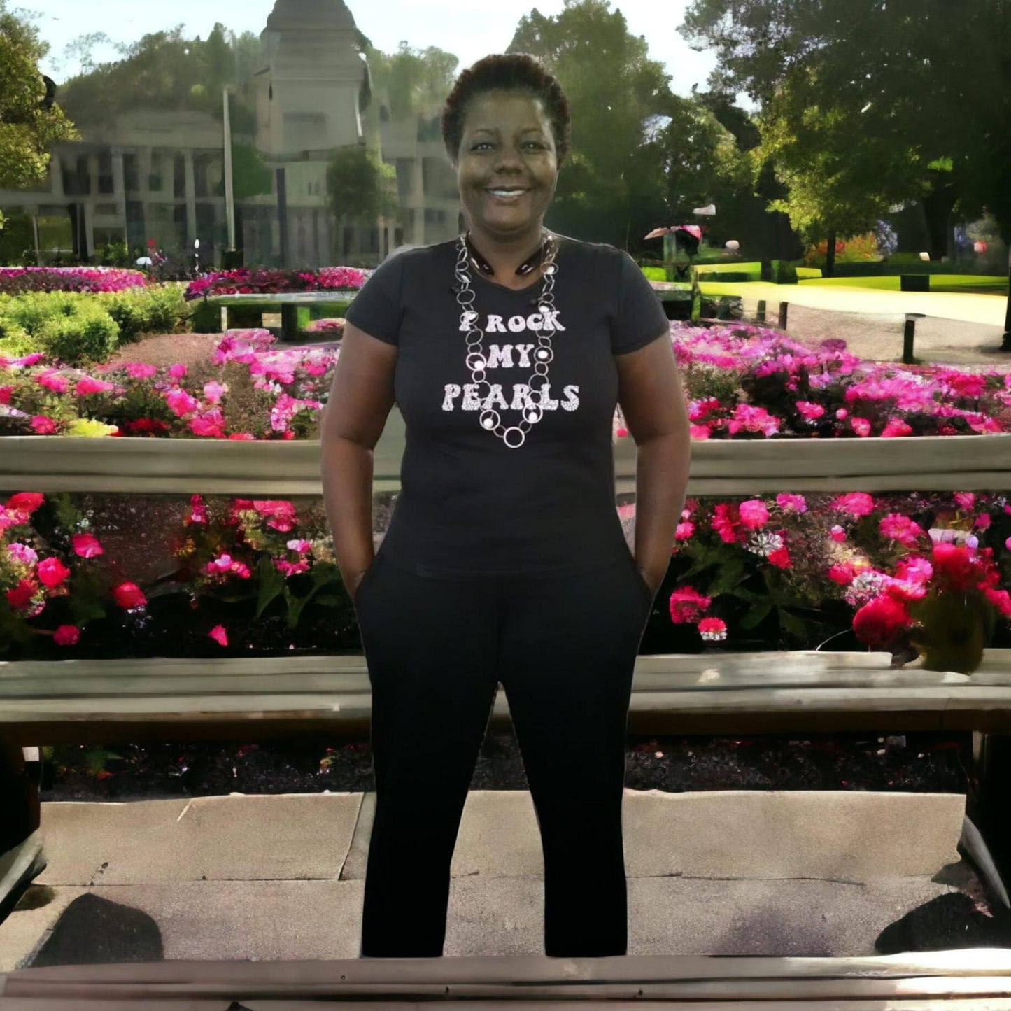 Person wearing a black t-shirt with text standing in front of a garden with pink flowers.