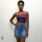 Woman wearing a tie-dye tube top and denim skirt against a plain background
