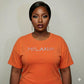 Woman wearing an orange Melanin Unisex T-Shirt with rhinestone "MELANIN" text, celebrating Black pride.