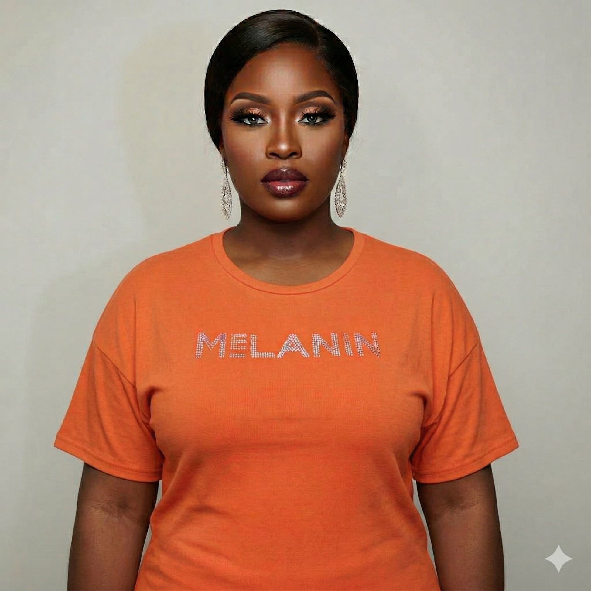 Woman wearing an orange Melanin Unisex T-Shirt with rhinestone "MELANIN" text, celebrating Black pride.