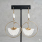 Brass hoop earrings with white carved bone fan and teardrop beads on a black display.