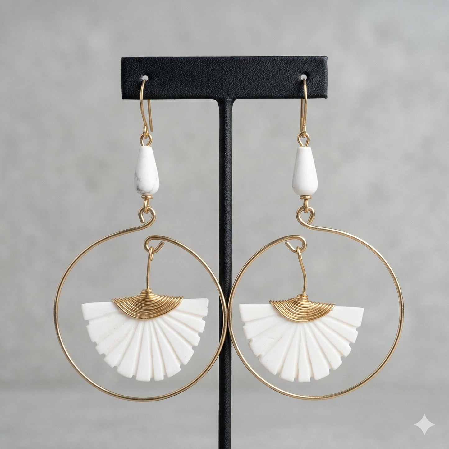 Brass hoop earrings with white carved bone fan and teardrop beads on a black display.