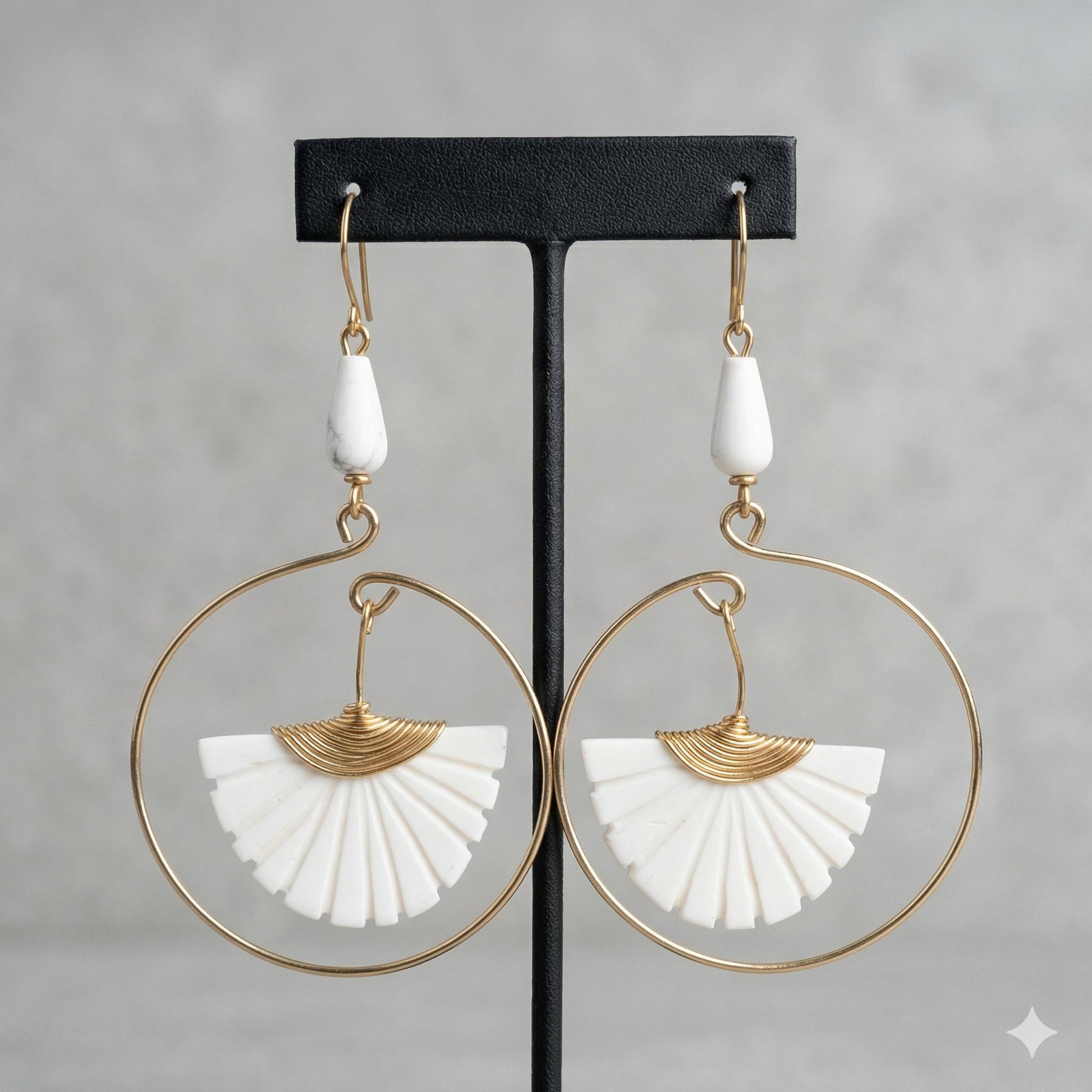 Brass hoop earrings with white carved bone fan and teardrop beads on a black display.