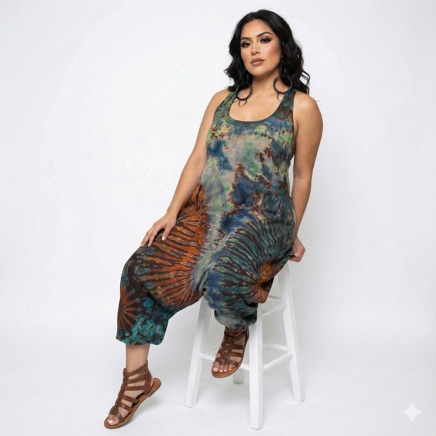 Woman wearing a tie-dye jumpsuit sitting on a white stool against a white background