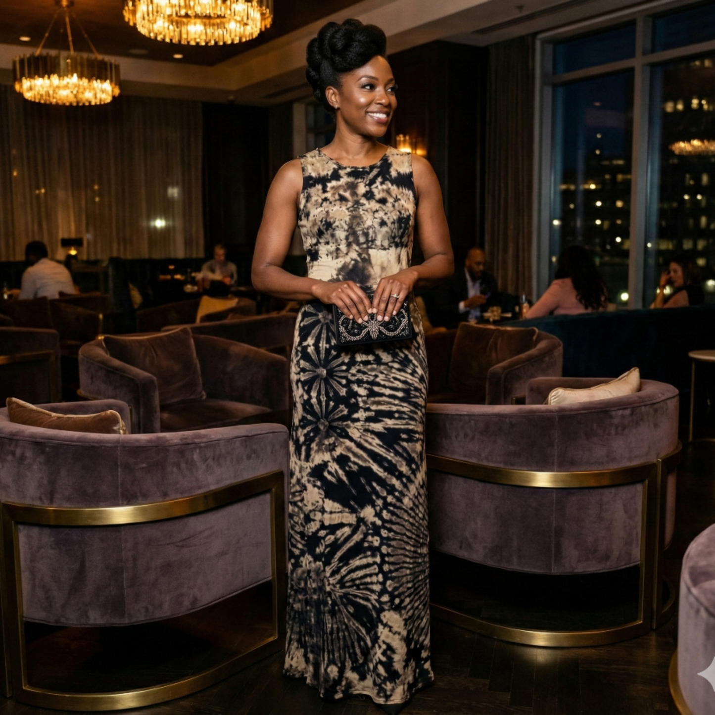 Woman in a tie dye dress standing in a stylish indoor setting with purple chairs and chandeliers.