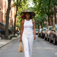 Woman walking down a street wearing a Batik colorful hat and white outfit
