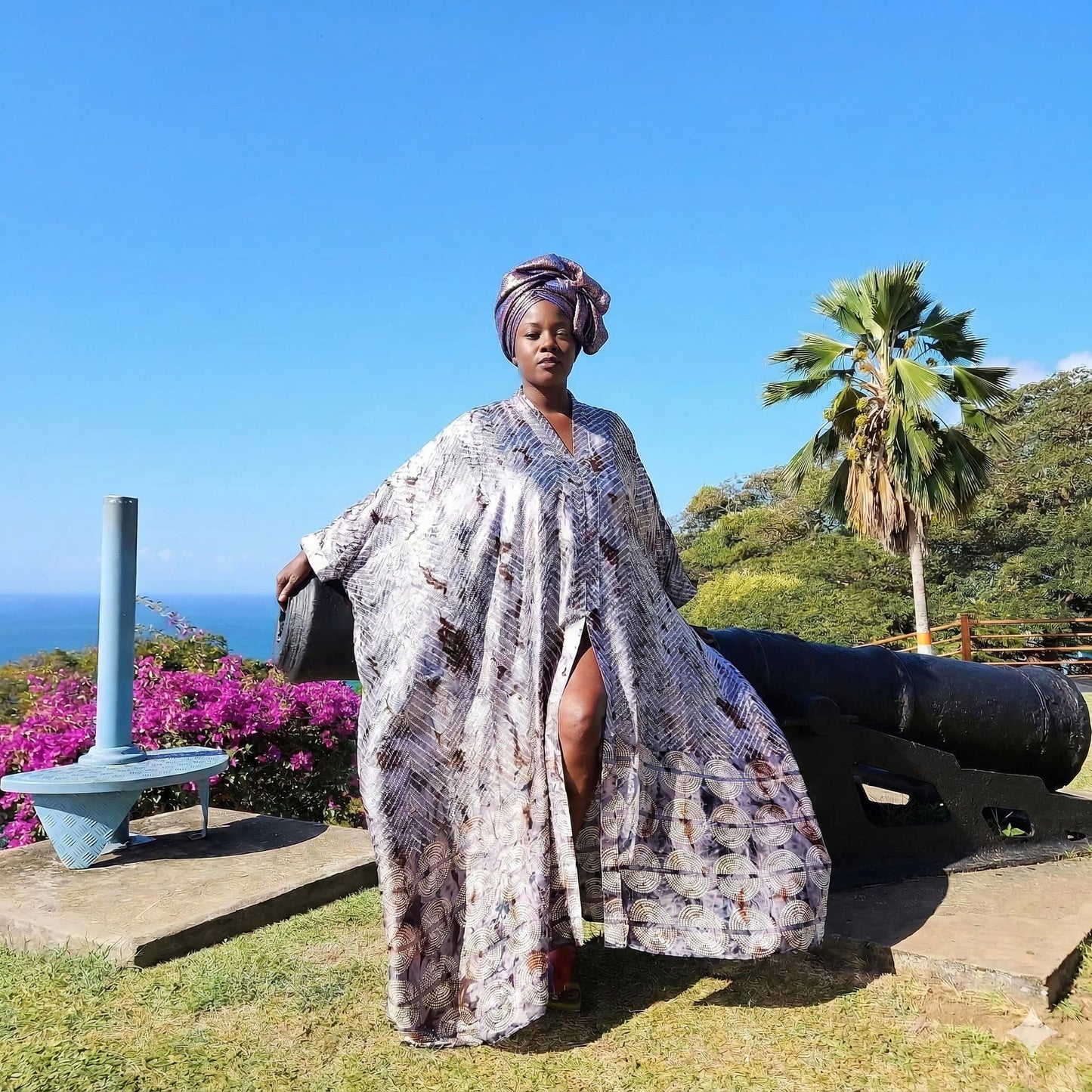 Woman in a kaftan standing next to a cannon with a scenic background