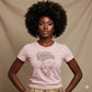 Woman in pink t-shirt with rhinestone head wrap design, gold earrings, and natural afro.