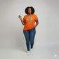 Woman in an orange Foxy Gold Afro rhinestone & reflective film t-shirt, blue jeans, and sneakers.