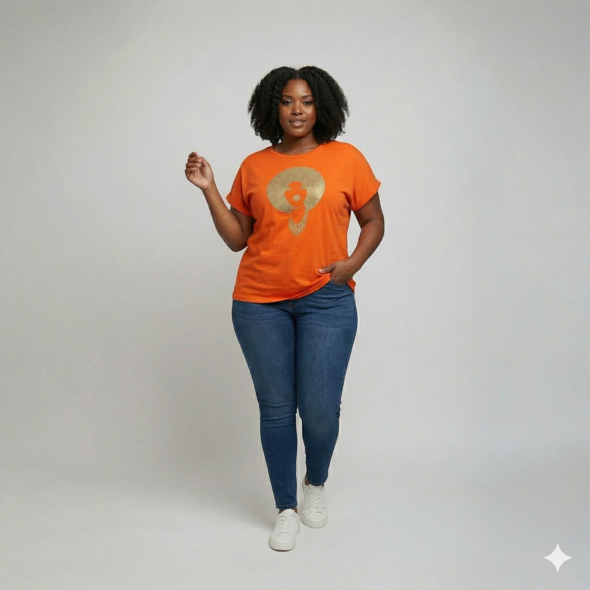 Woman in an orange Foxy Gold Afro rhinestone & reflective film t-shirt, blue jeans, and sneakers.