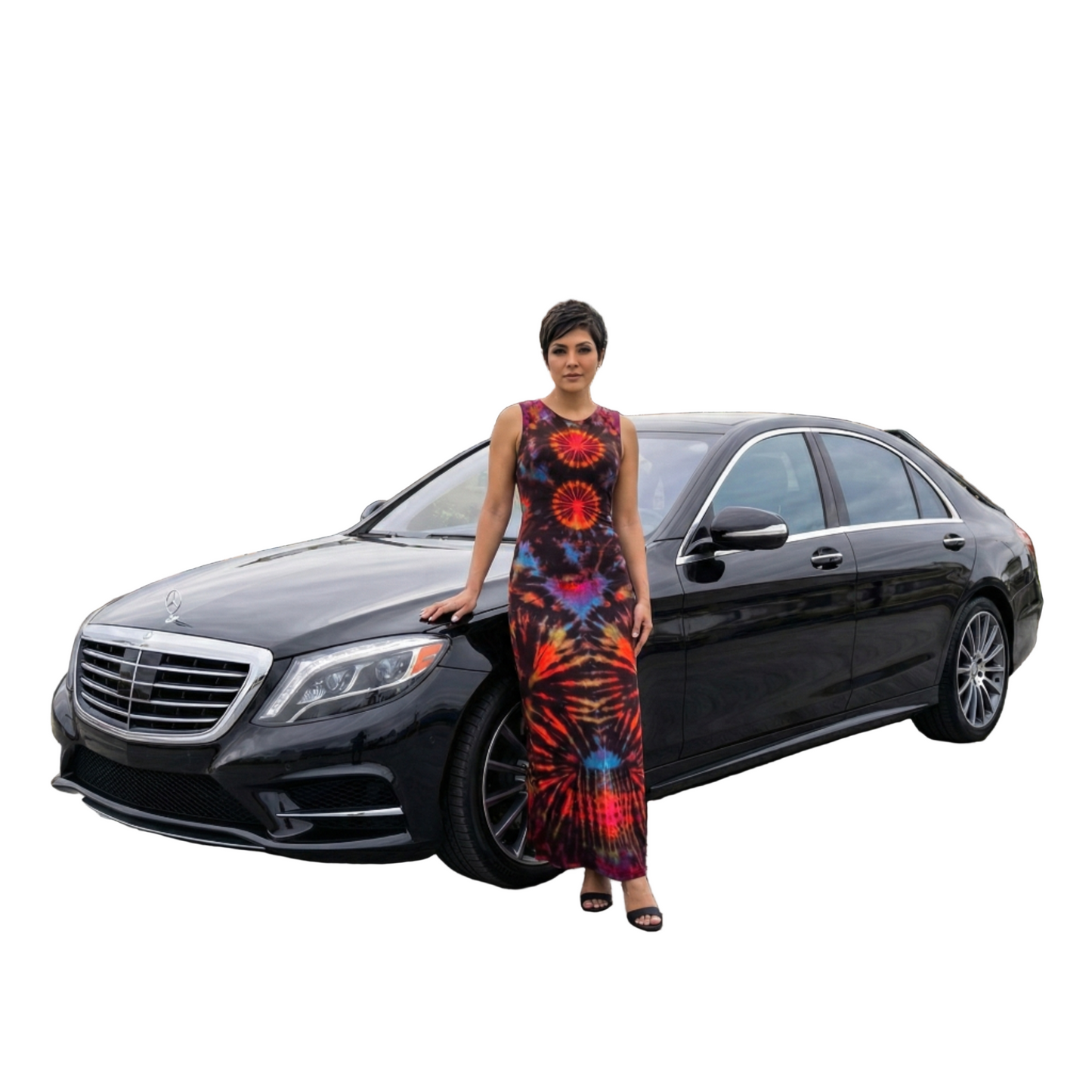 Woman in a tie dye dress standing next to a black Mercedes-Benz car on a city street.