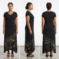A woman modeling a black maxi dress with a beige floral and geometric print concentrated at the hem.