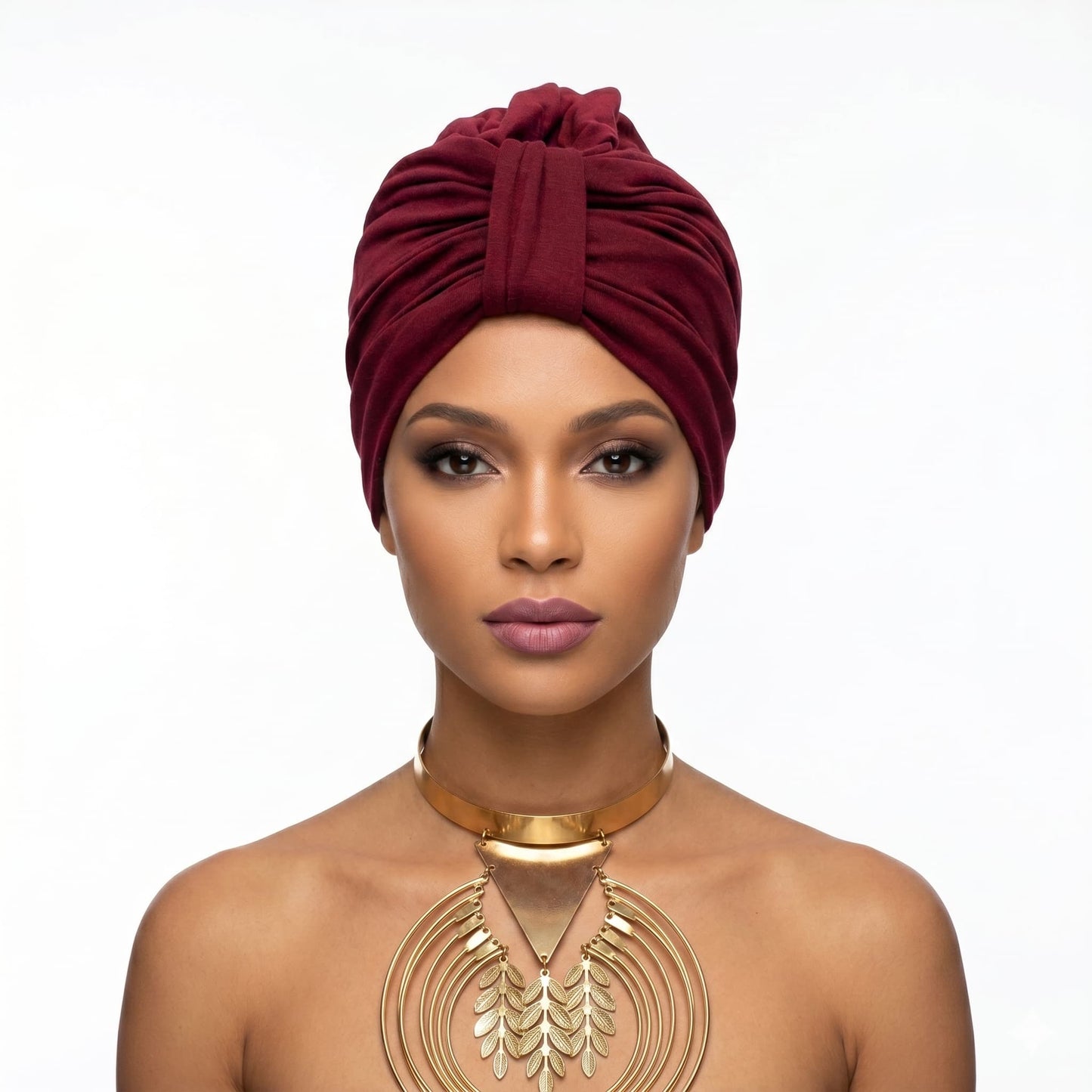Woman wearing a maroon turban and gold necklace on a white background