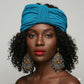 Woman wearing a blue turban and large earrings against a gray background