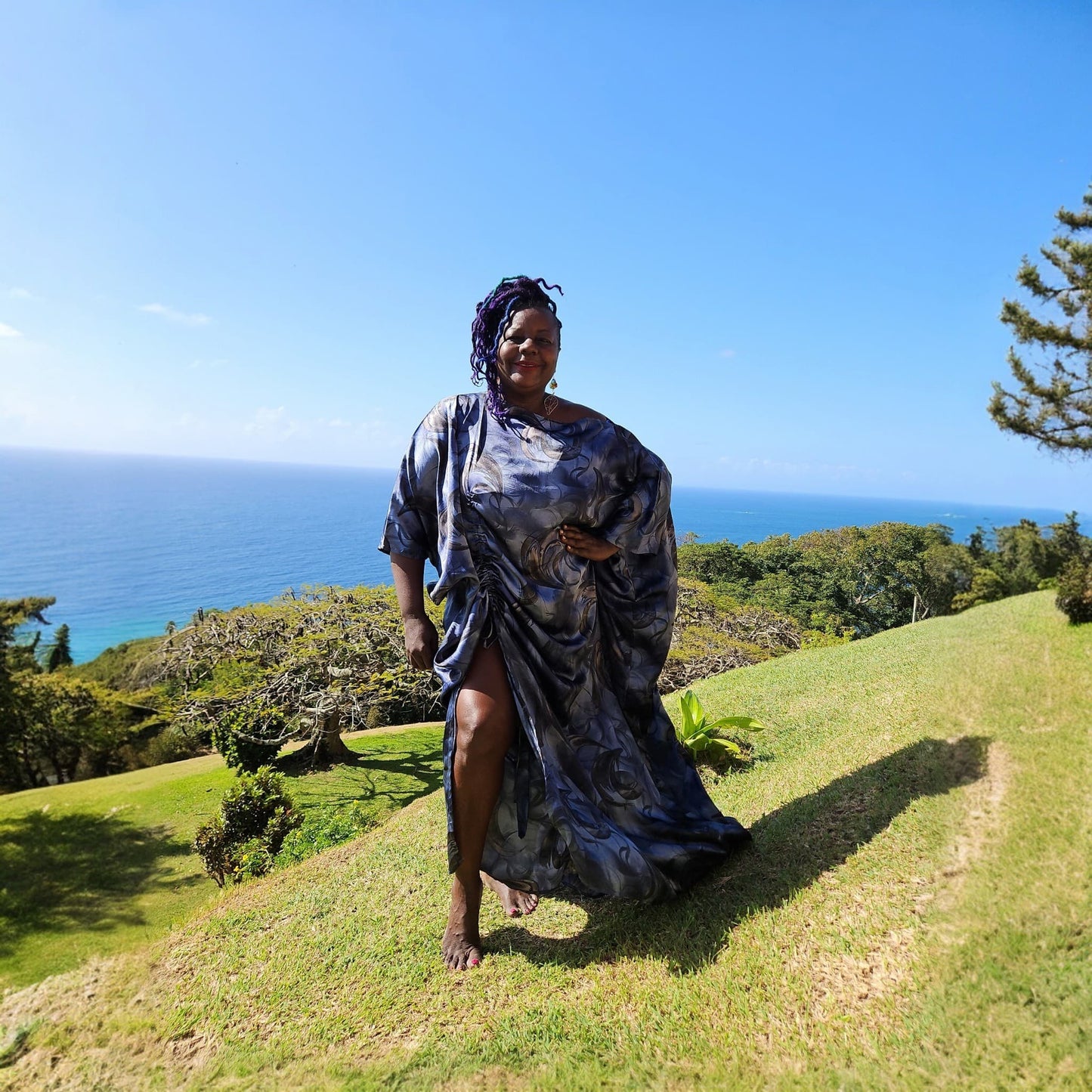 Woman in a blue Boubou dress standing on a grassy hill with ocean view