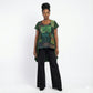 Woman wearing a green and black patterned top with black pants on a white background