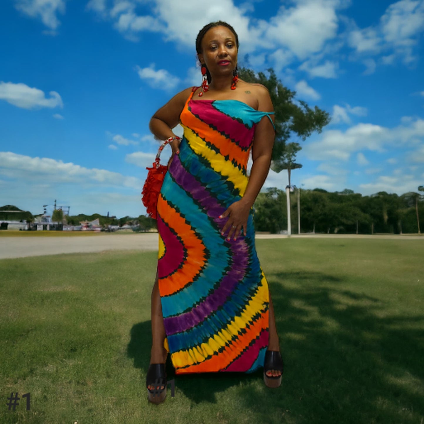 Woman wearing a colorful tie-dye dress standing outdoors on a grassy area with a blue sky.-Sanjules