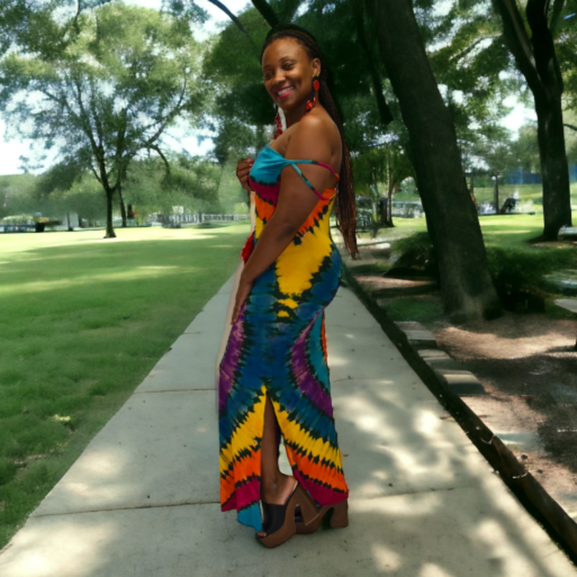 Woman in a colorful tie-dye dress standing on a sidewalk with trees and grass in the background-Sanjules