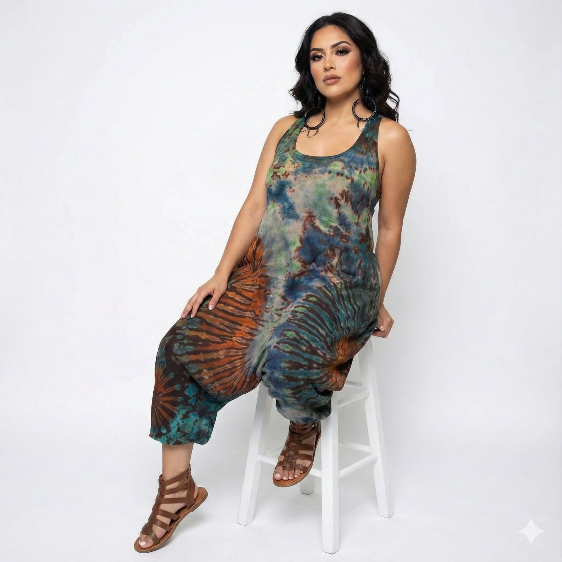 Woman wearing a tie-dye jumpsuit sitting on a white stool against a white background SanJules