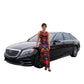 Woman in a tie dye dress standing next to a black Mercedes-Benz car on a city street. SanJules