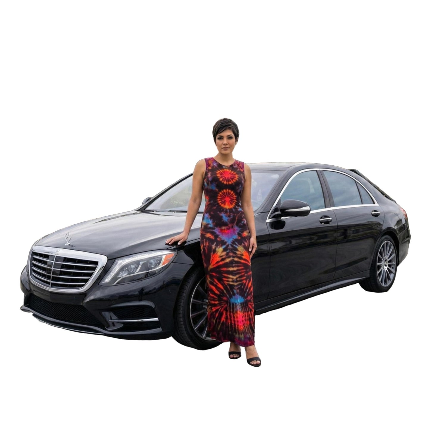 Woman in a tie dye dress standing next to a black Mercedes-Benz car on a city street. SanJules