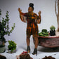Woman in a colorful dress standing among potted plants on a white background. SanJules