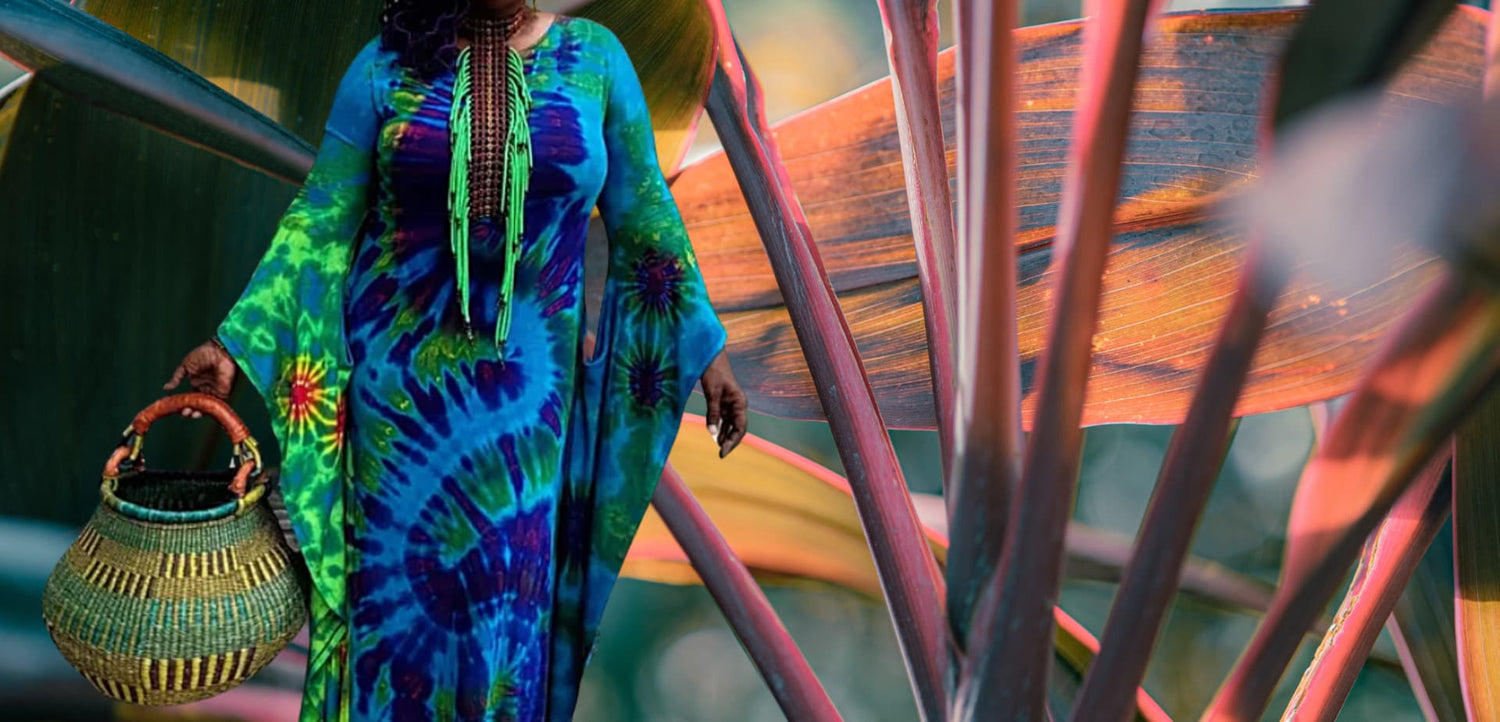 Person wearing a colorful tie-dye outfit holding a woven basket, standing in front of a textured wall-Sanjules.