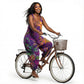 Woman in a colorful tie-dye harem jumpsuit riding a bicycle with a basket on a white background 