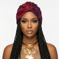 Woman wearing a red and purple turban  with braided hair and gold jewelry on a white background