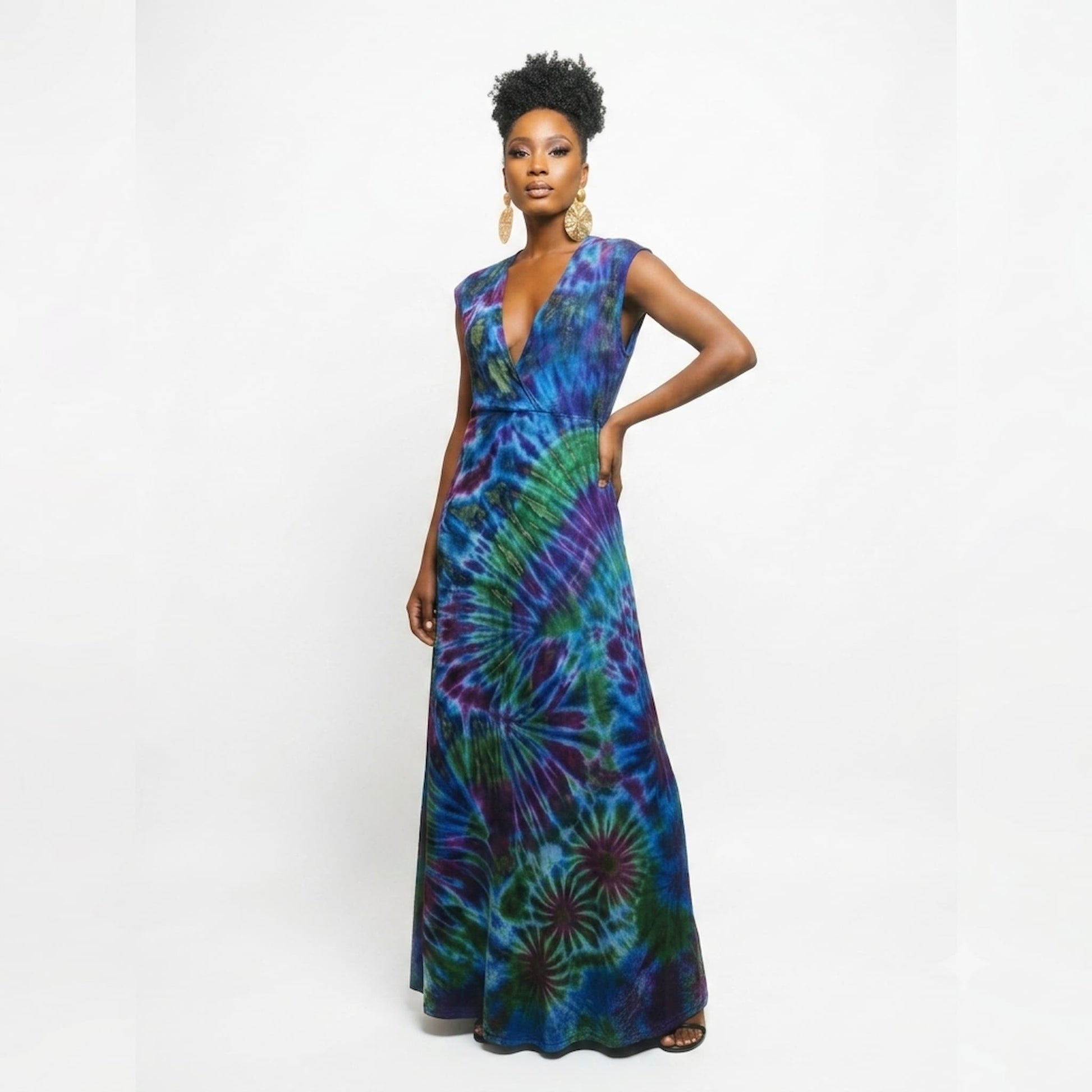 A woman modeling a sleeveless, floor-length wrap maxi dress with a vibrant tie-dye pattern