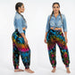 Two women wearing colorful tie-dye pants and a denim shirt on a white background