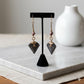 Kenyan brass, cowrie shell, and hand-carved bone drop earrings on a black display stand.