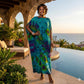 Woman in a tie-dye dress standing by a pool with ocean view