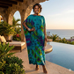 Woman in a tie-dye dress standing by a pool with ocean view
