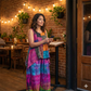 Woman in a colorful patch top standing in a cozy restaurant with brick walls and string lights.