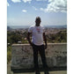 Man in white Black Power Fist Rhinestone T-Shirt, black pants, outdoors with city and ocean view.