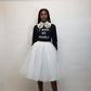 Person wearing a black t shirt with text and a white tulle skirt against a plain background