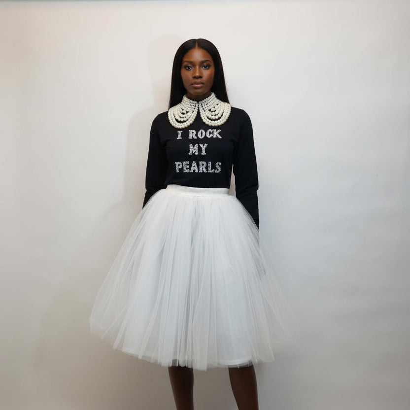 Person wearing a black t shirt with text and a white tulle skirt against a plain background
