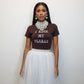 Woman wearing a brown shirt with 'I Rock My Pearls' text, white pearls, and a white tulle skirt on a white background.