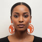 Woman wearing large, round orange wooden earrings with cut-out Africa map silhouettes.