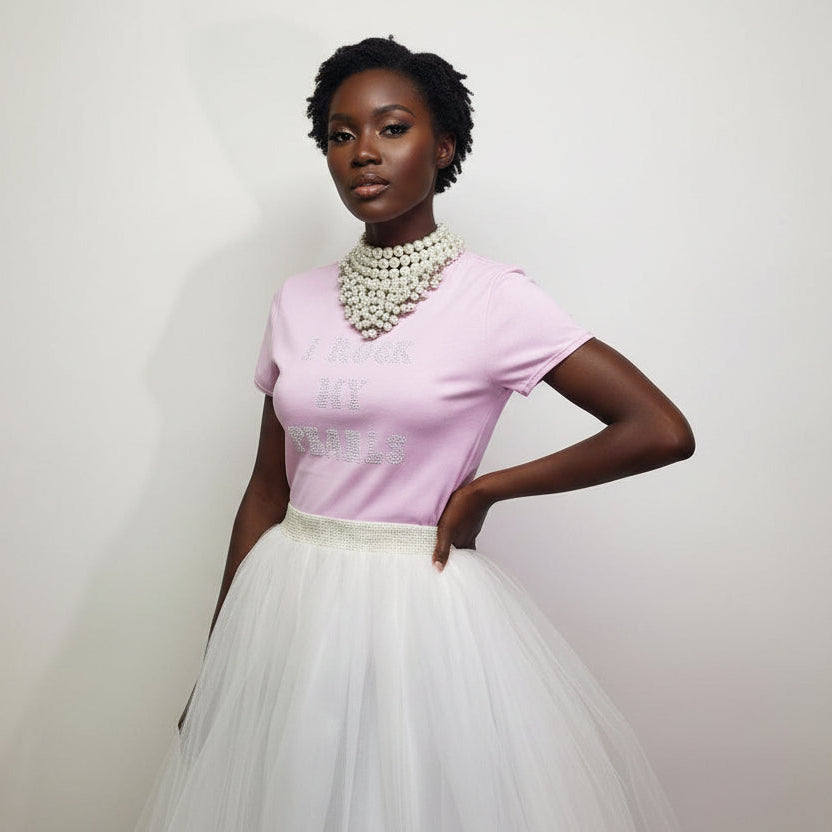 Woman wearing a pink top and white skirt with a pearl necklace against a plain background