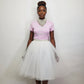 Woman wearing a pink t shirt and white tulle skirt with a plain background