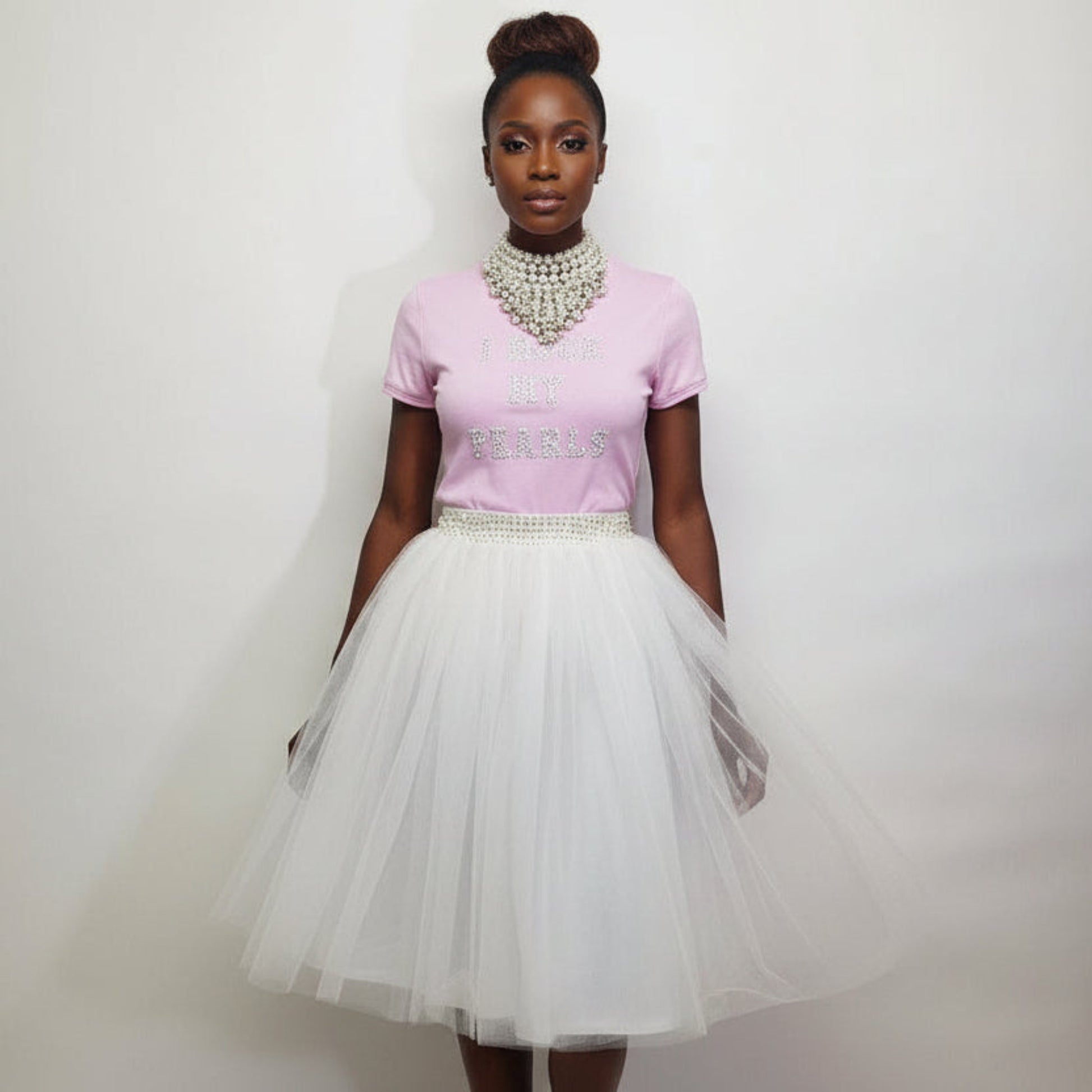 Woman wearing a pink t shirt and white tulle skirt with a plain background
